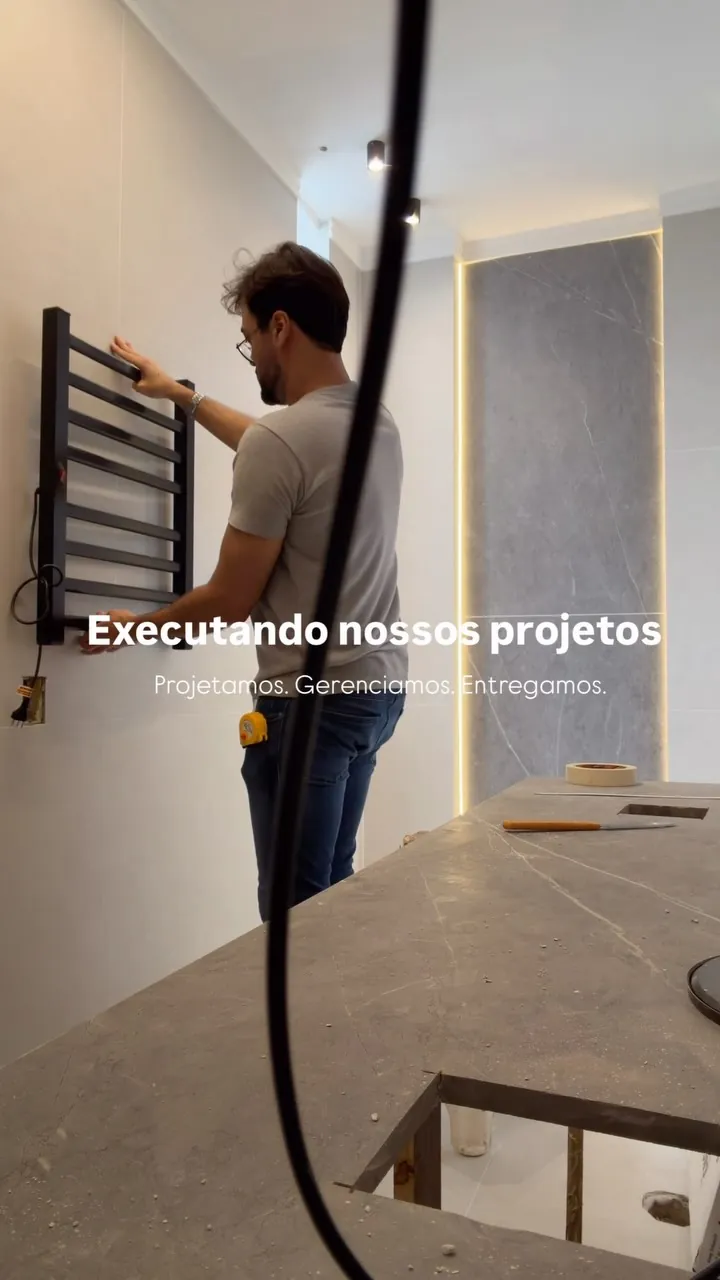 Kaká Pitombo instalando um toalheiro em banheiro em obra, com a legenda “Executando nossos projetos — Projetamos. Gerenciamos. Entregamos.”